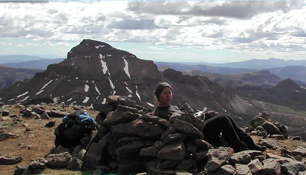 Suzy on Wetterhorn Peak signing the summit register, with Uncompahgre Peak in the background.